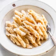 Penne with vegan white sauce on a white plate on a light grey background.