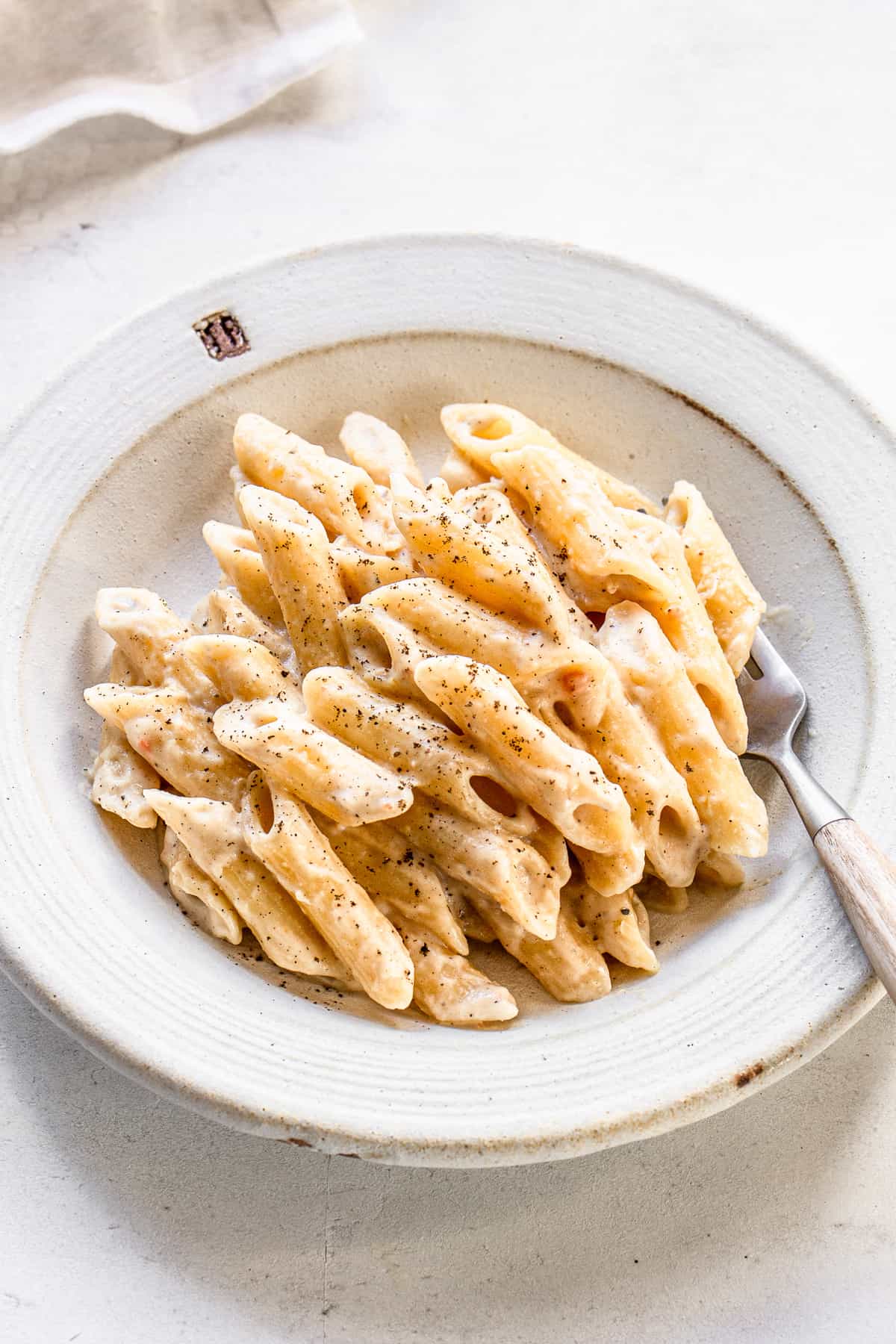 Penne with white sauce on a white ceramic plate with a fork.