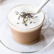 Lavender flavored latte in a ribbed glass cup with milk foam and topped with lavender buds.