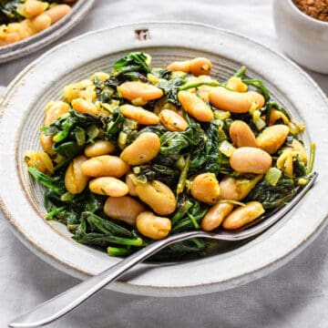 Sauteed white beans with cooked spinach in a grey ceramic plate.