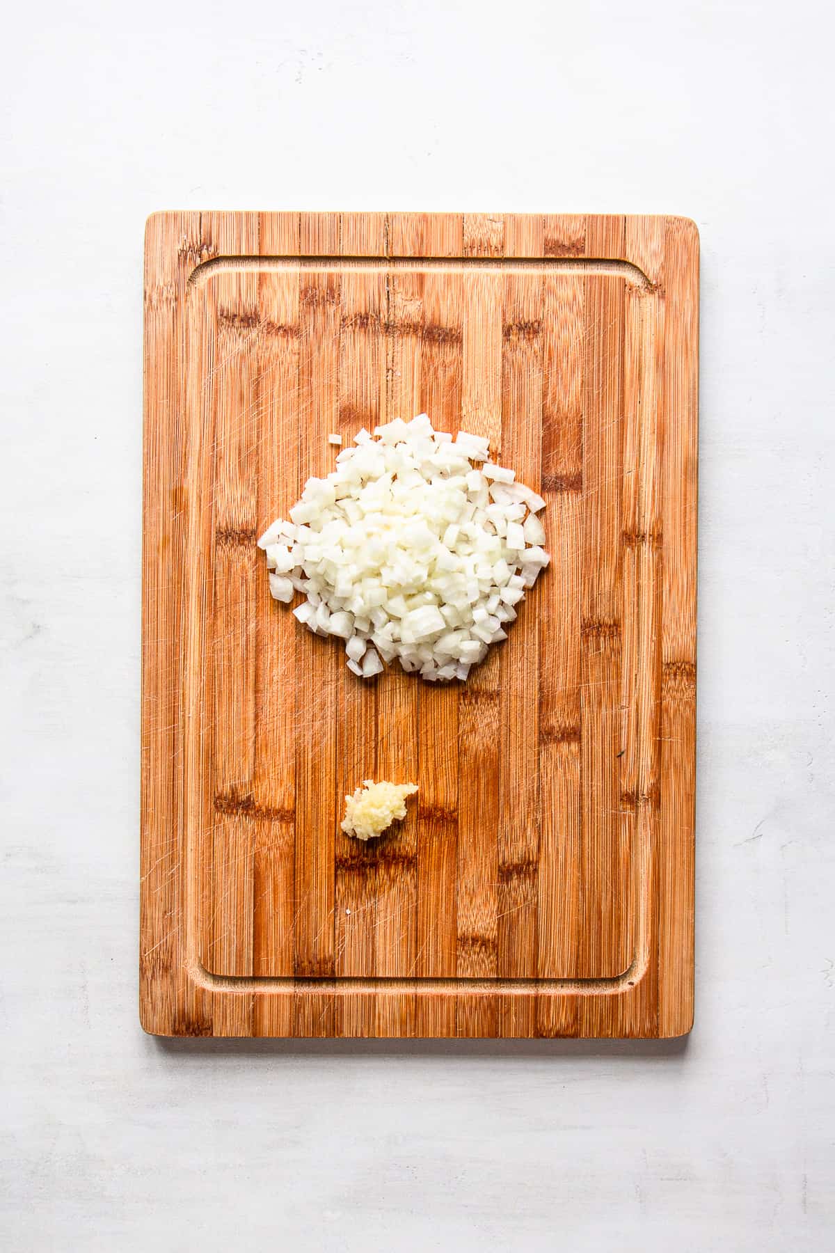 Minced onion and crushed garlic on a wooden cutting board.