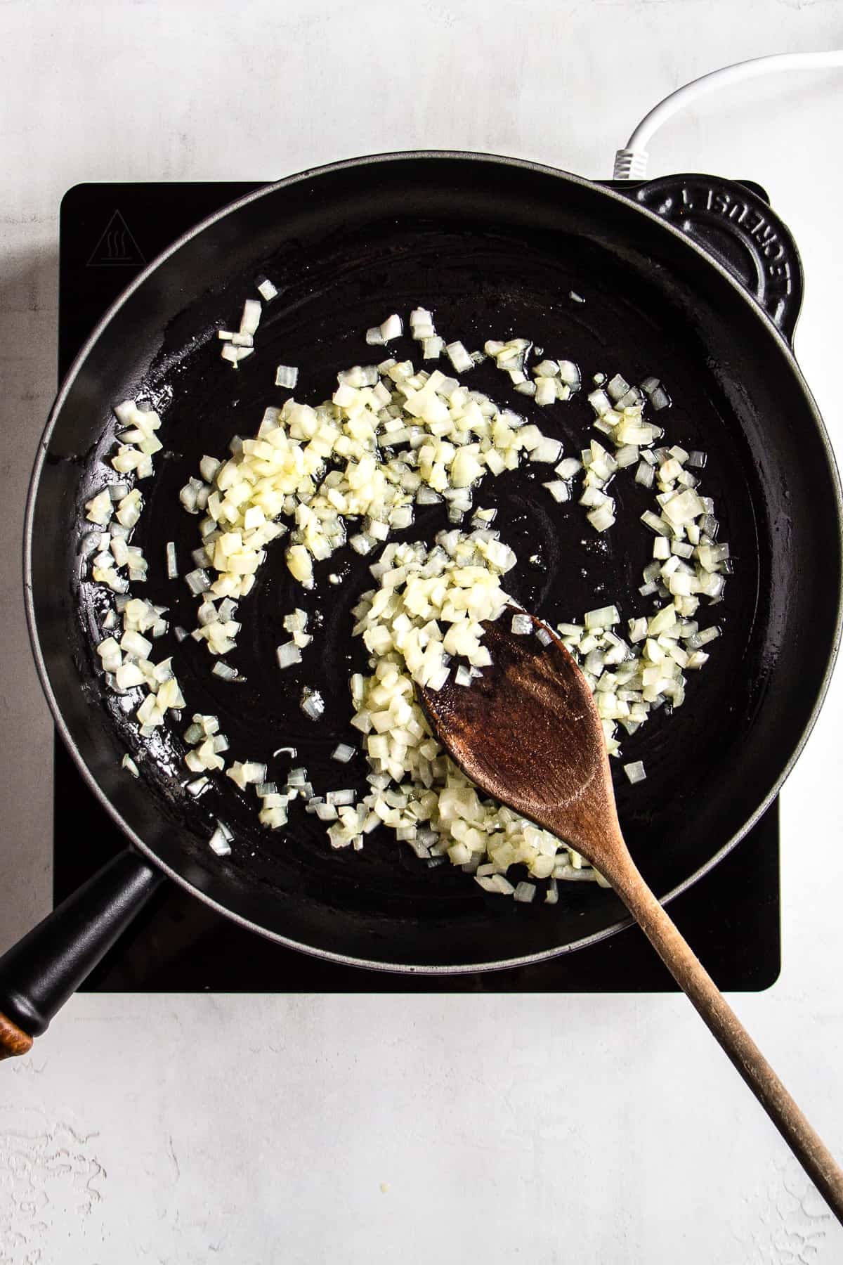 Sauteed onion and garlic in a black pan on a portable electric stove.