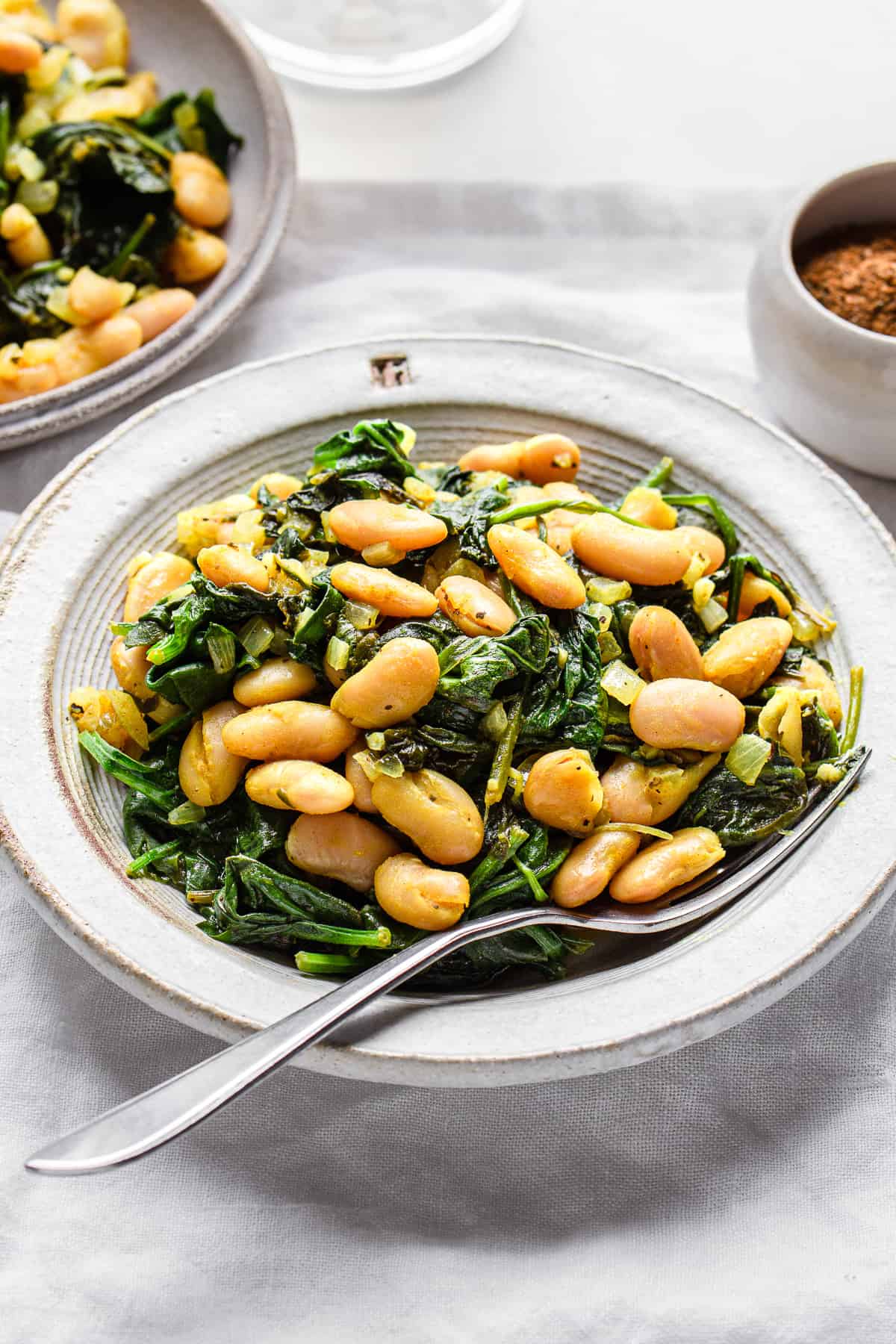 Lemon spinach white beans on a grey ceramic plate with an antique fork.