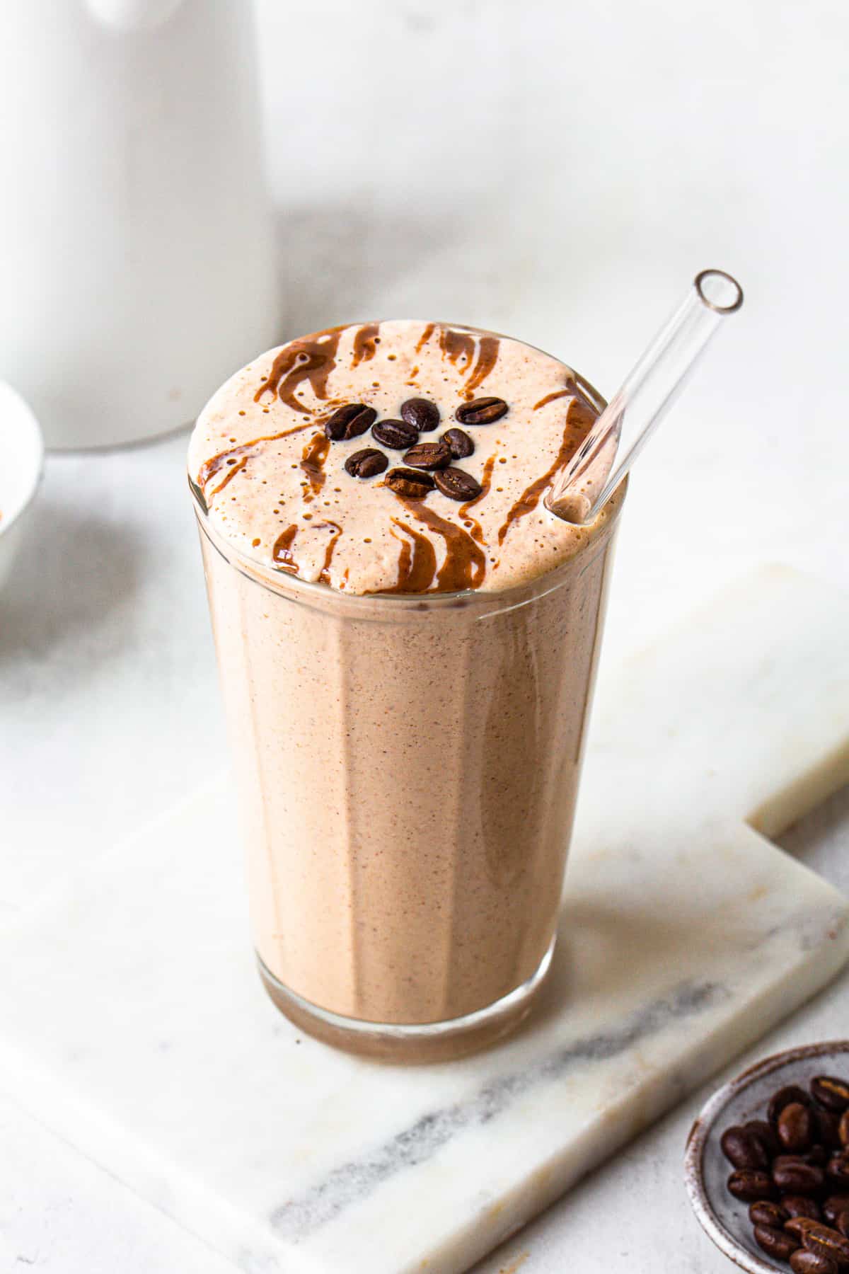 Brown coffee smoothie in a ribbed glass topped with almond butter and coffee beans.