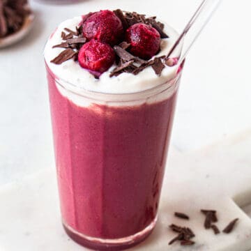 Red smoothie topped with yogurt, chocolate shaves and 3 frozen cherries.