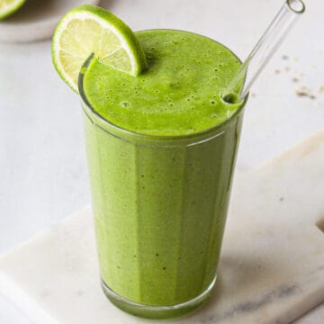 Bright green smoothie in a ribbed glass with a lime wheel on the rim of the glass.