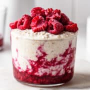 Small glass with overnight oats with raspberries as the bottom and as a garnish.