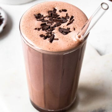 Dark brown chocolate smoothie with some air bubbles on top and chocolate shavings.