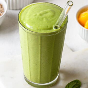 Creamy bright green smoothie in a ribbed glass with a glass straw.