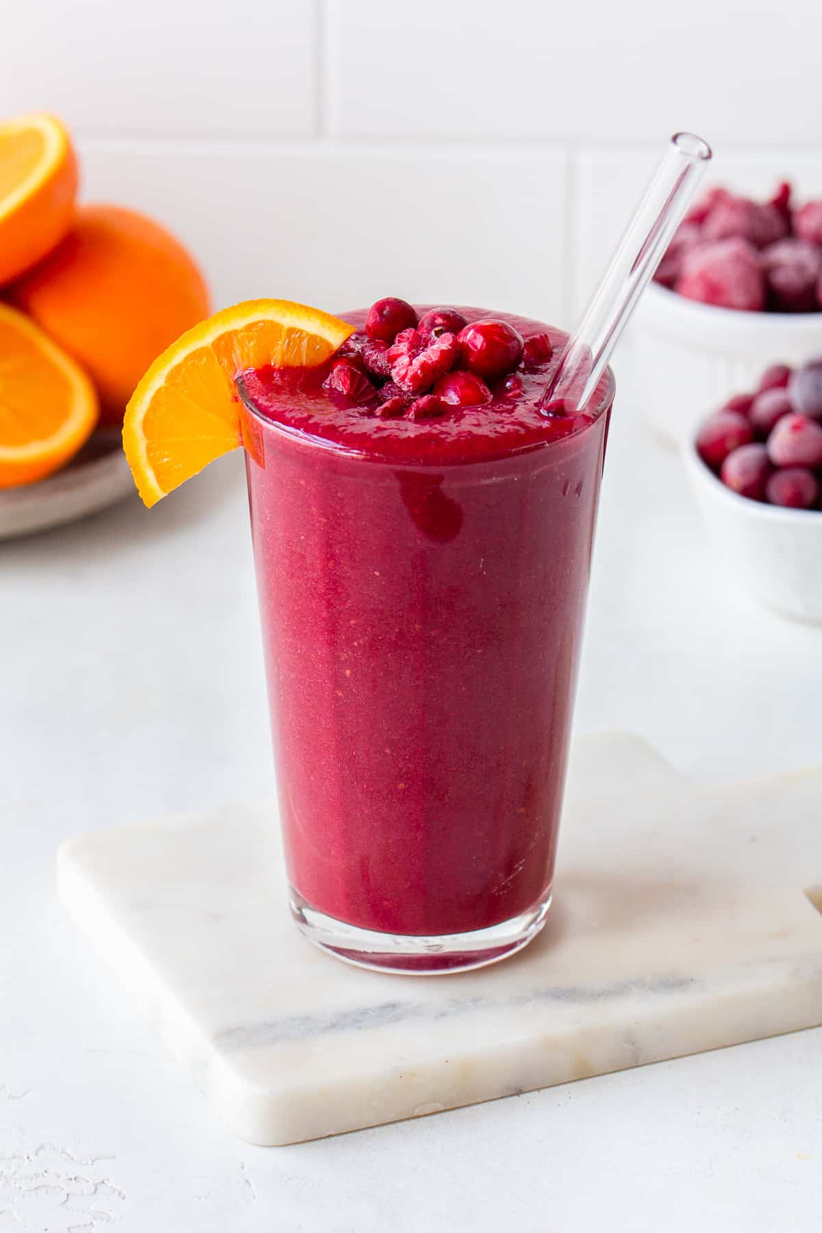 Pink smoothie topped with raspberries, cranberries and a half an orange slice.