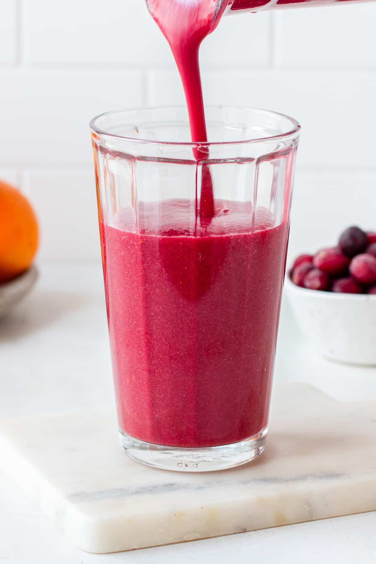 Blender pouring a bright pink smoothie in a tall glass.