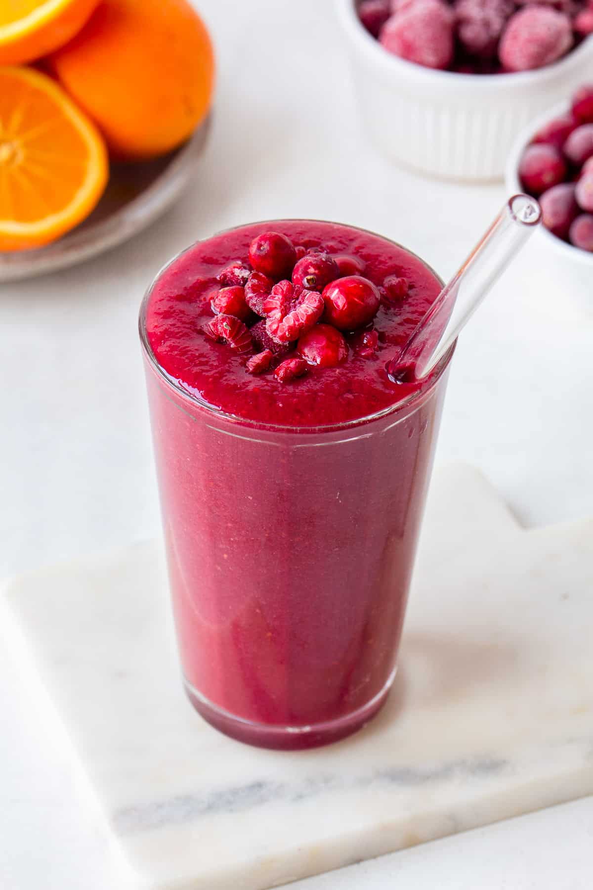 Pink smoothie topped with raspberries and cranberries with oranges in the background.