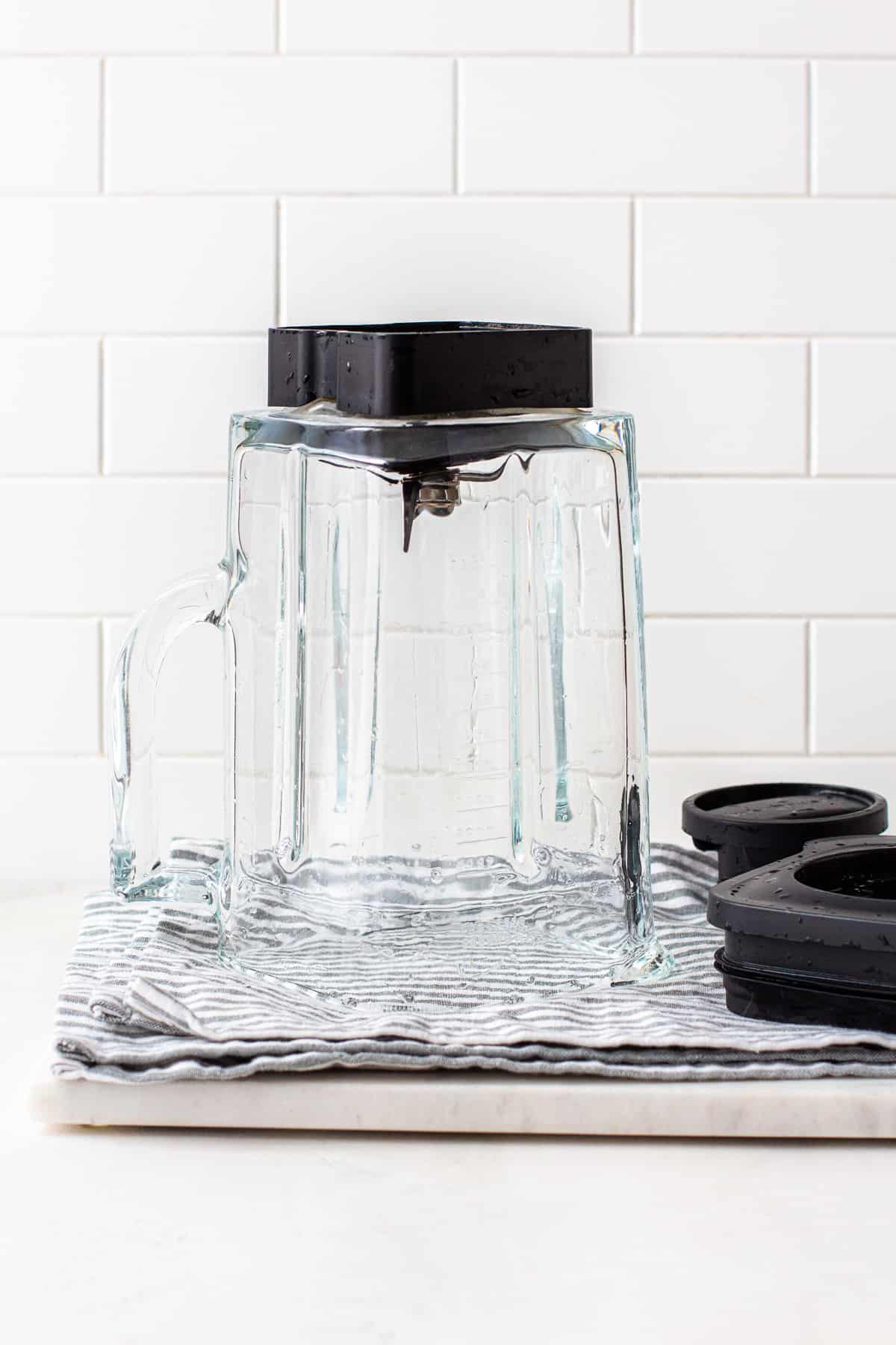 Kitchenaid blender jar and lid drying on a blue and white towel.