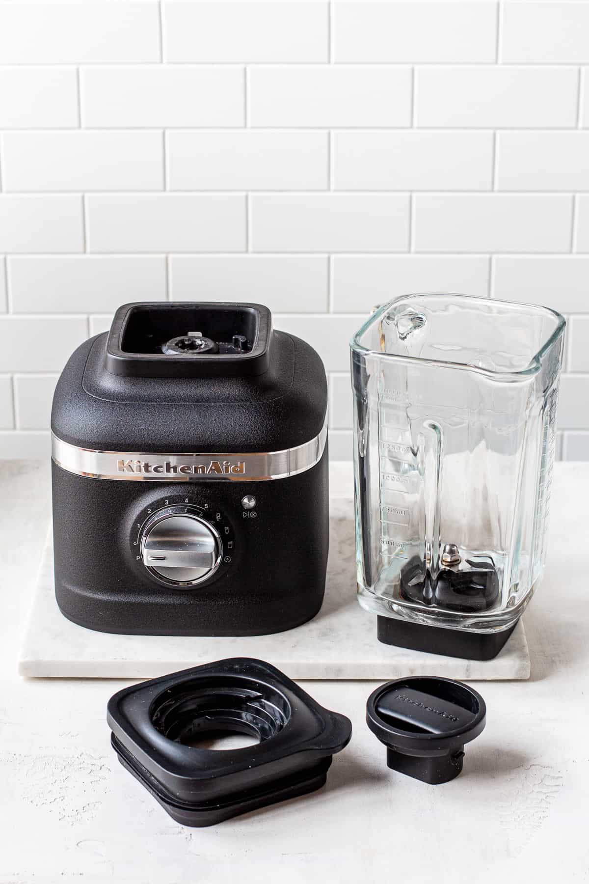 Motor base, glass blender jar and black plastic lid on a marble platter.