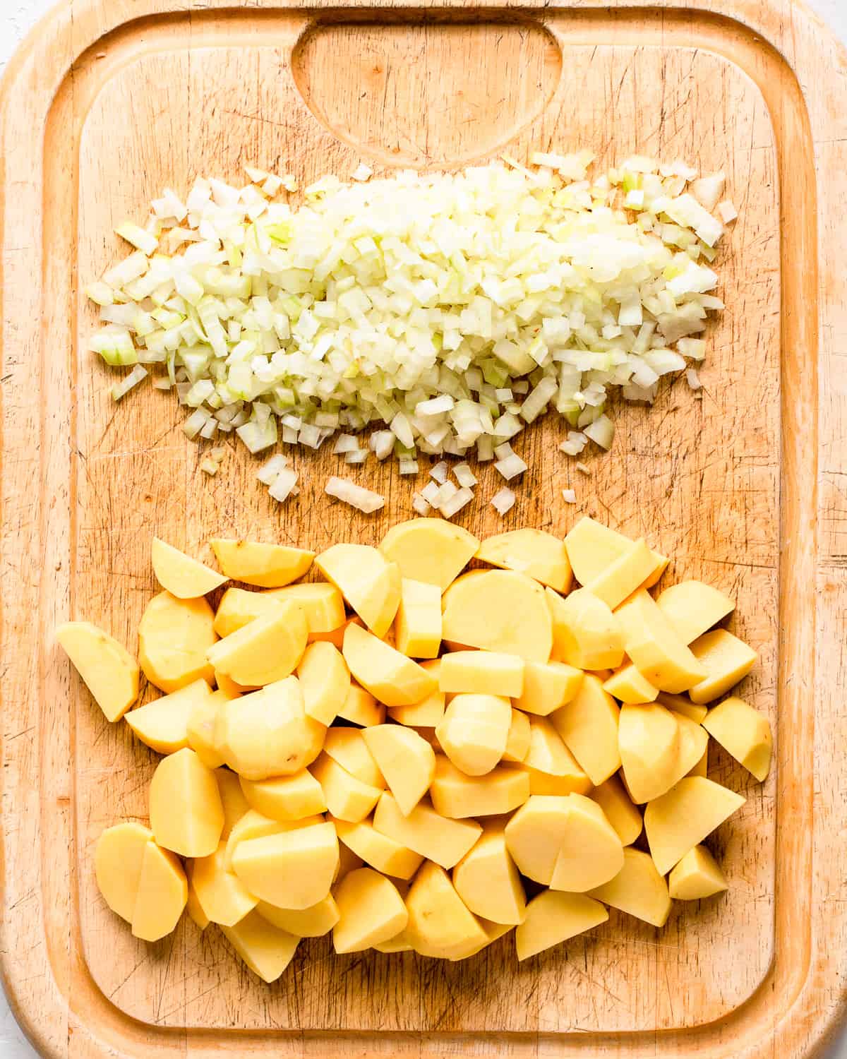 Minced onion and potato chunks on a large wooden cutting board.