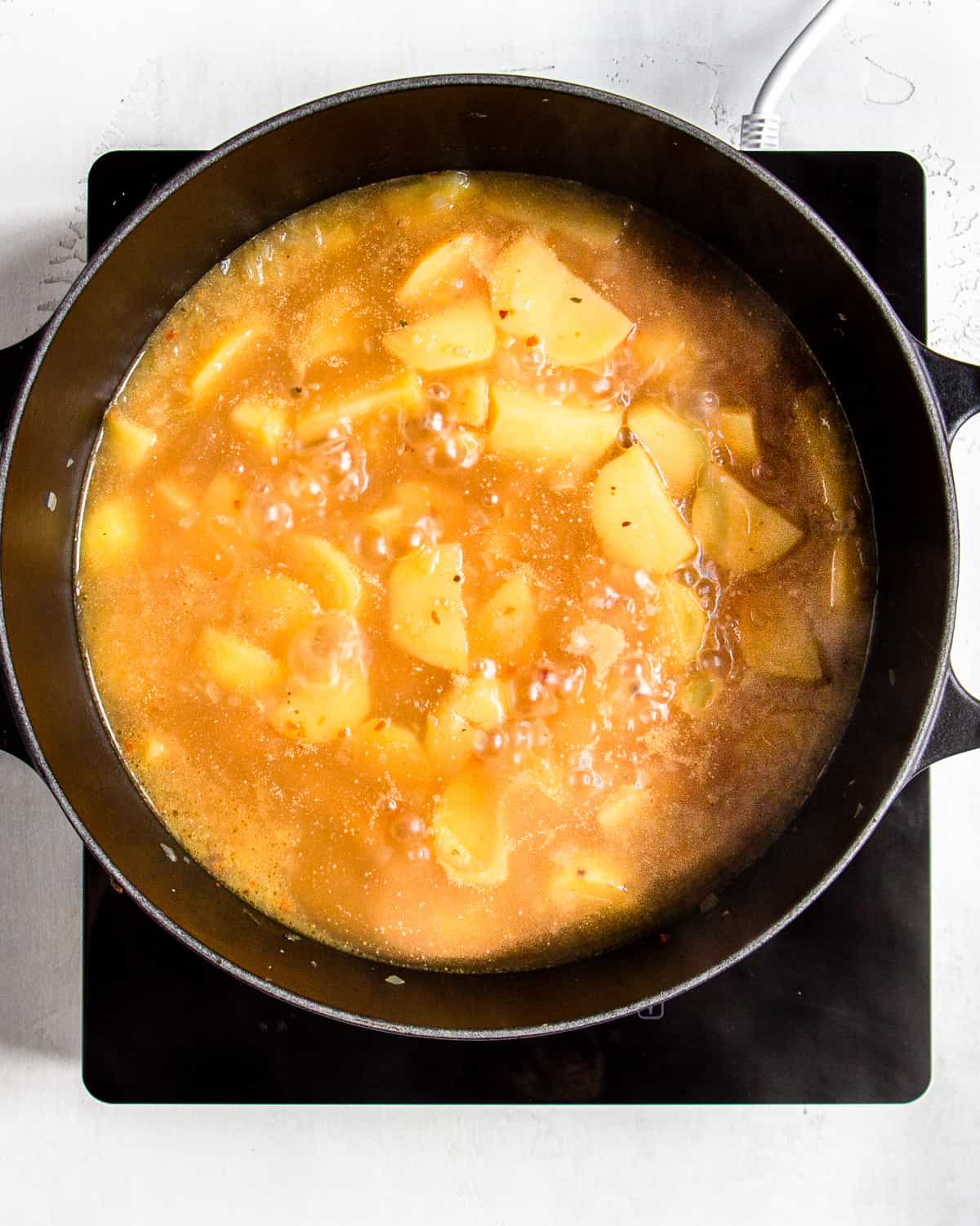 Simmering potato soup in a black Dutch oven.