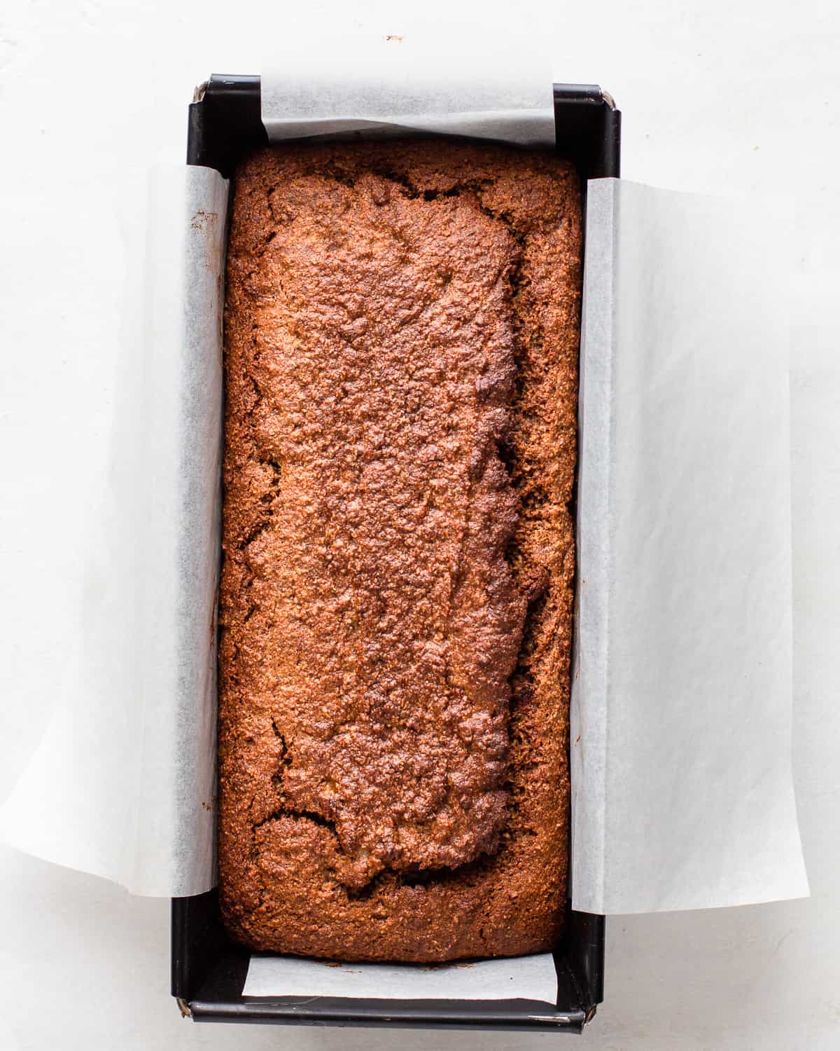 Baked banana bread with a golden brown crust in a black loaf pan.