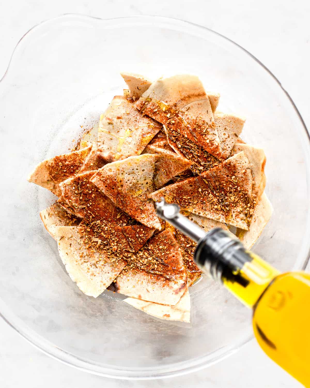 Glass bottle drizzling oil over tortilla triangles.