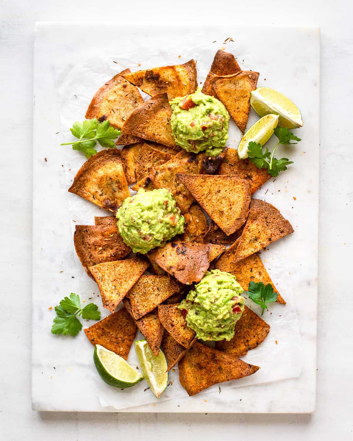 Baked nachos from tortillas on a white marble platter with guacamole, lime and fresh cilantro.