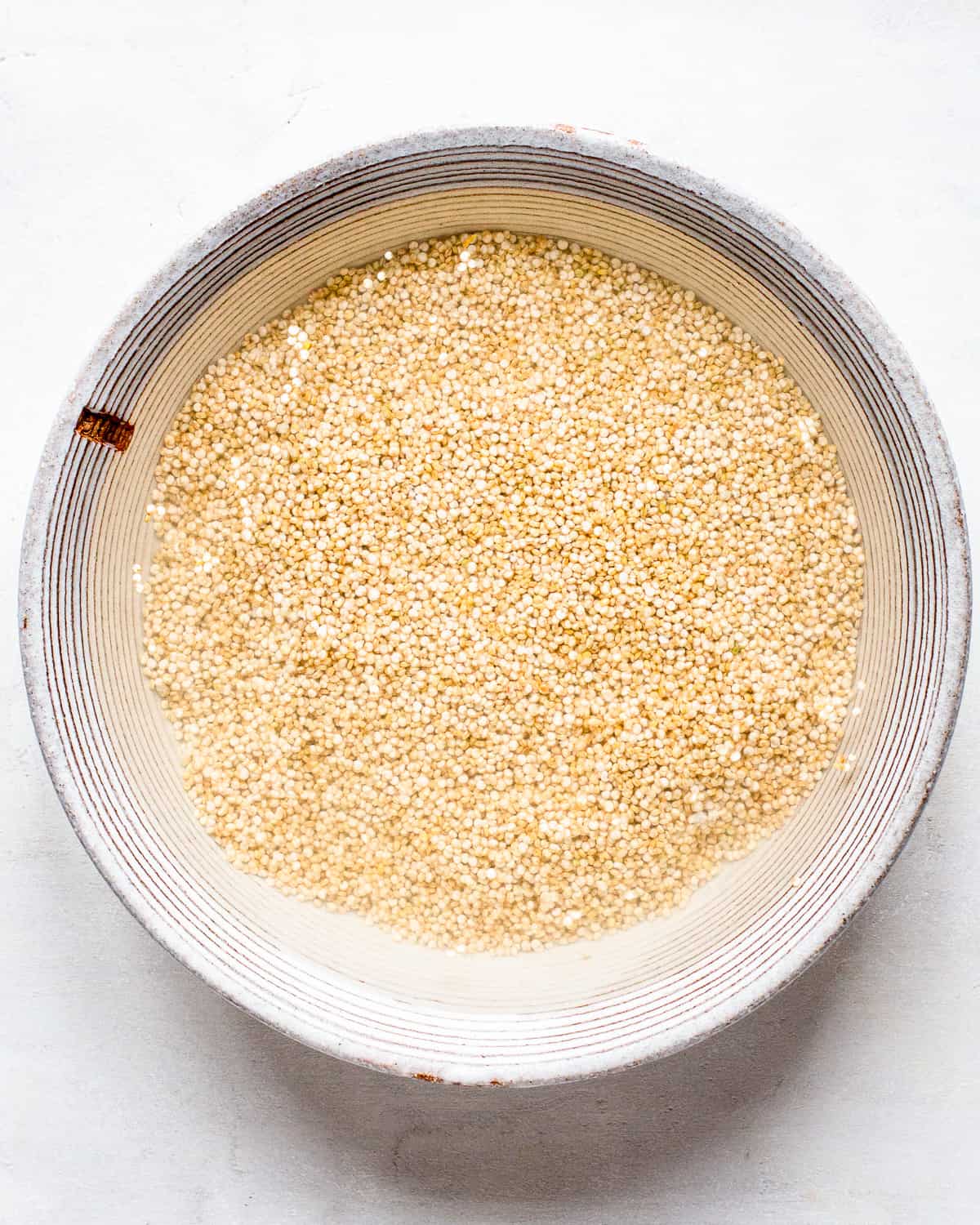 Quinoa soaked in water in a grey ceramic bowl.
