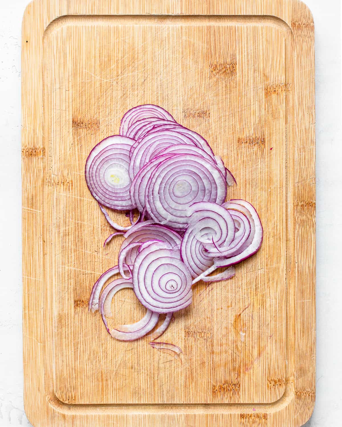 Sliced red onions on a wooden cutting board.