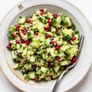 Millet tabbouleh with parsley, cucumber and pomegranate seeds on a grey ceramic plate.