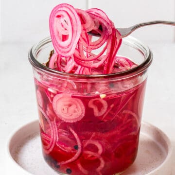 Fork taking red wine vinegar pickled red onions from a jar.