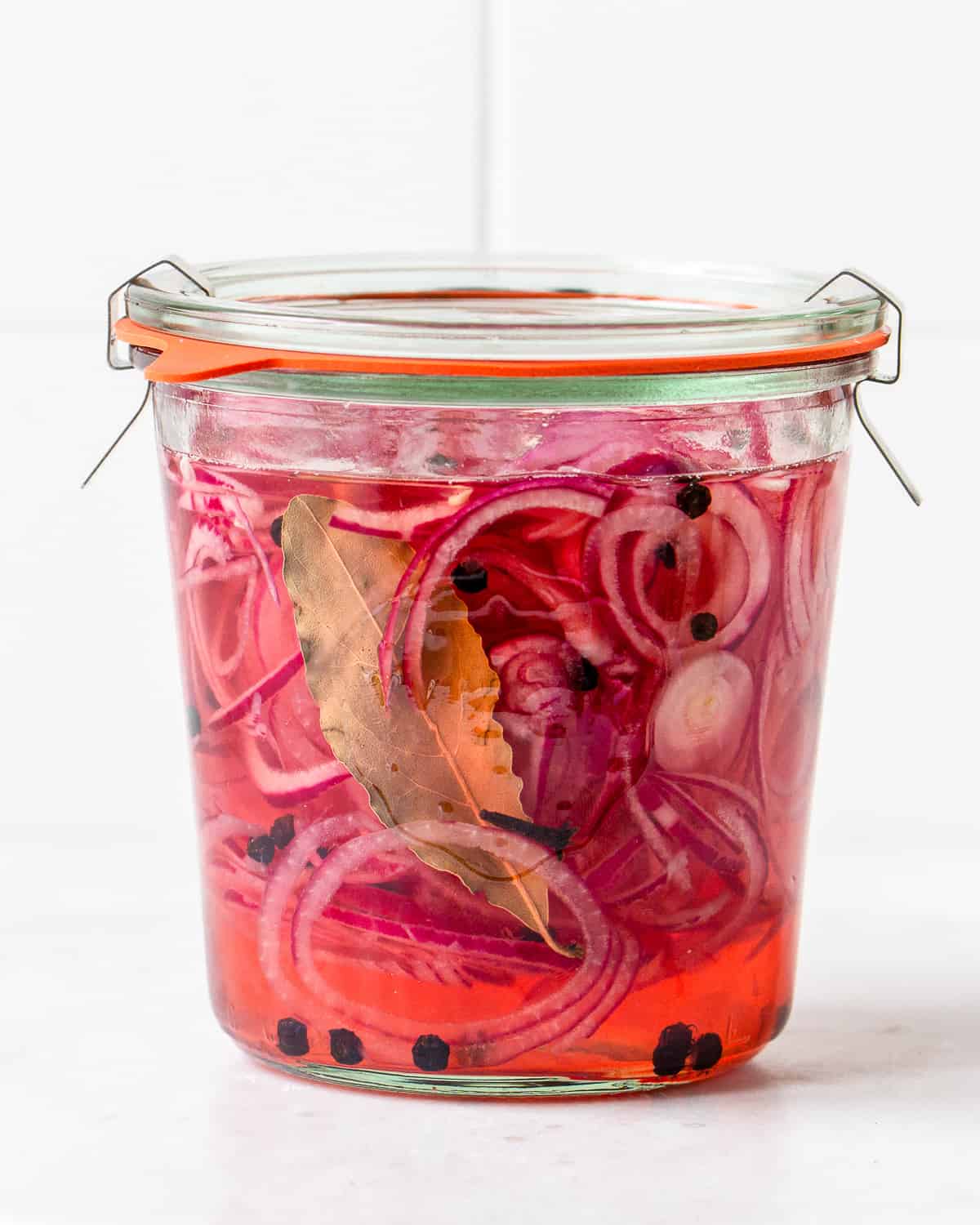 Sliced red onions in vinegar brine with spices in a glass jar.