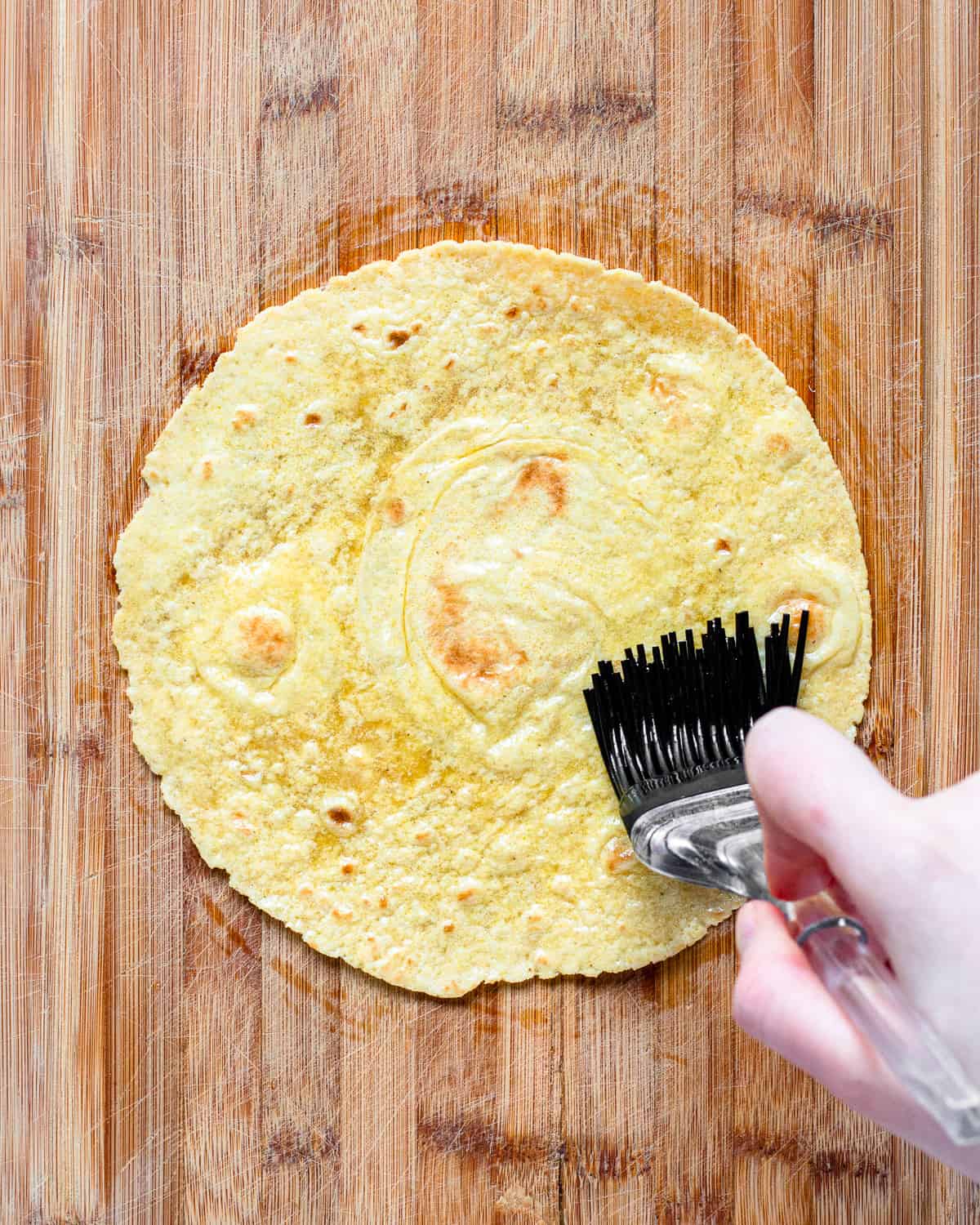 Hand brushing oil onto a yellow tortillas with a silicon brush.