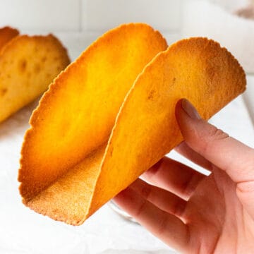 Hand holding a baked taco shell made from a tortilla.