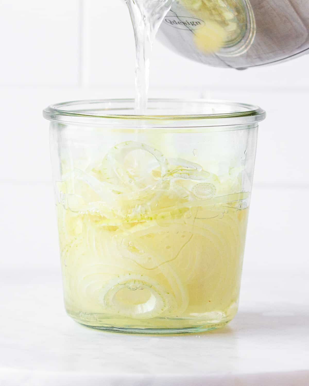 Sliced yellow onions in a white wine vinegar brine in a glass jar.