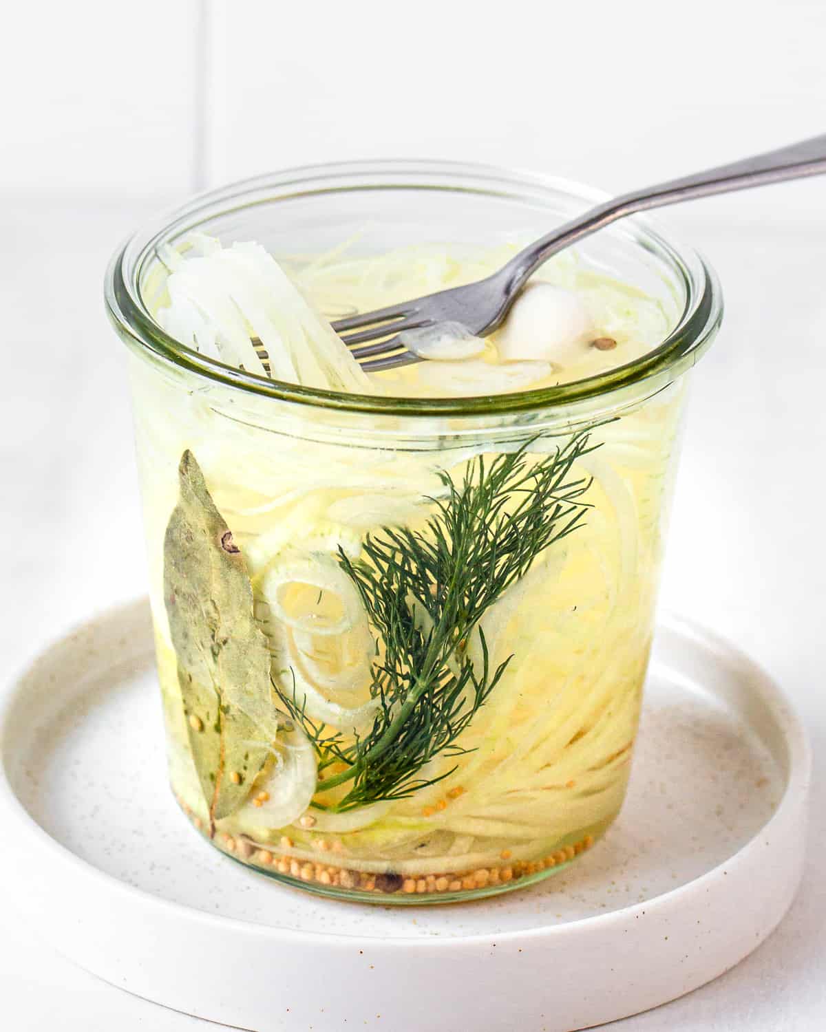 Fork taking yellow pickled onions from a jar.