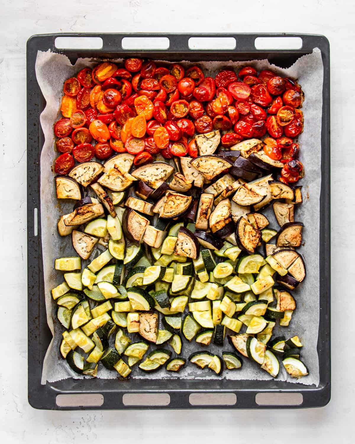 Roasted zucchini, eggplant, and cherry tomatoes on a baking sheet.