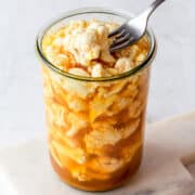 Fork taking curry pickled cauliflower florets out of a glass jar.