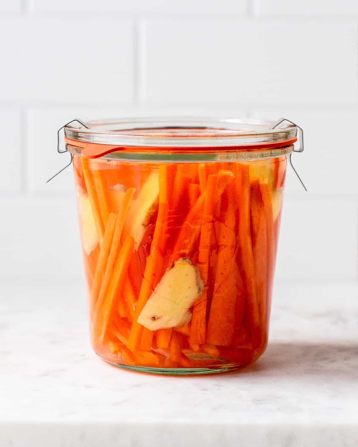 Closed Weck jar filled with carrot sticks, ginger slices and a vinegar pickling brine.