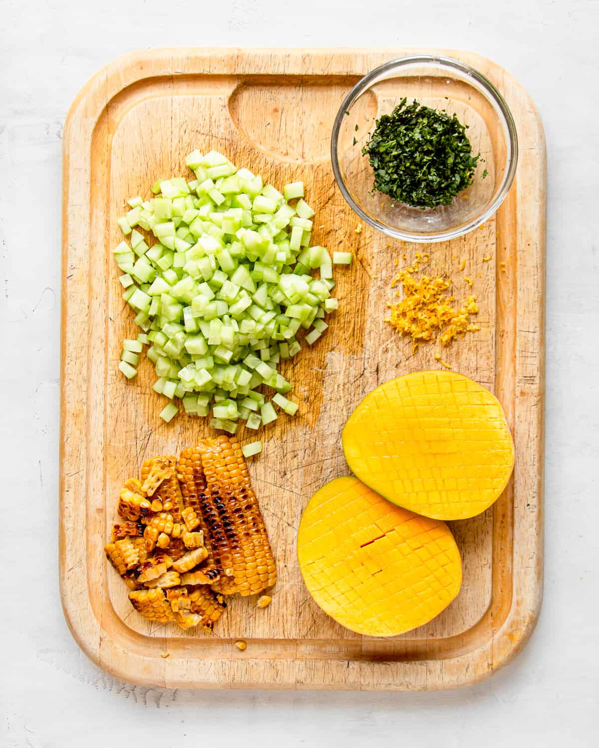 Diced cucumber, mango, and grilled corn on a wooden cutting board.