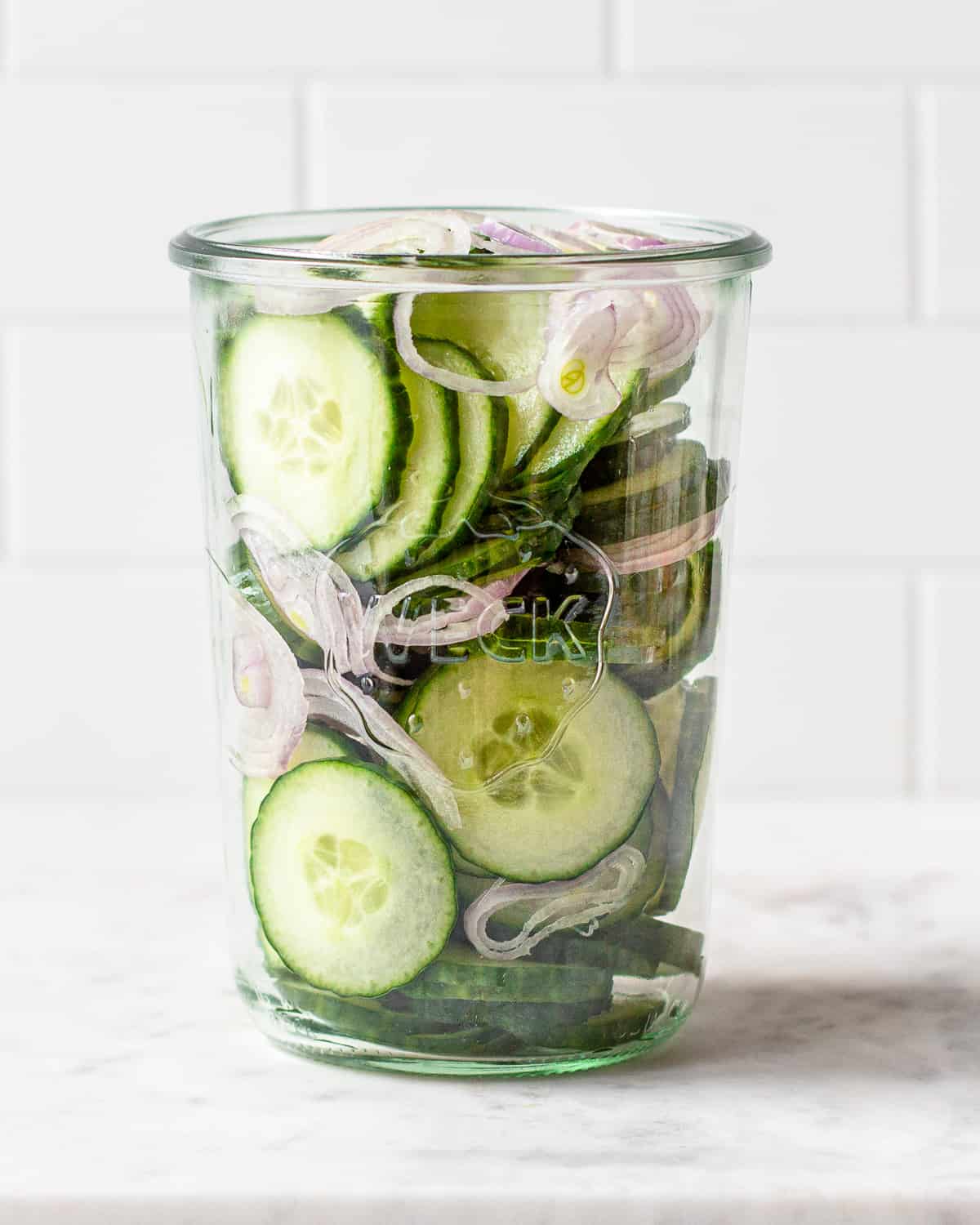 Sliced cucumbers and shallots in a tall Weck jar.