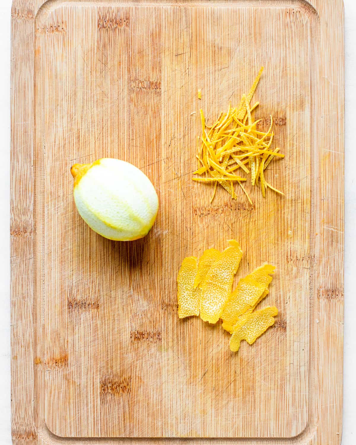 Zested lemon and lemon strips on a wooden cutting board.