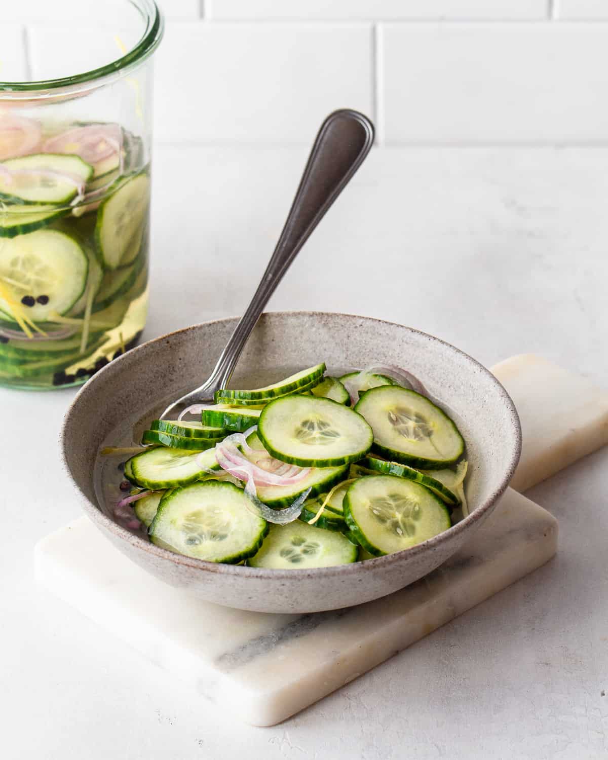 Pickled cucumber salad with shallots and lemon zests in a grey ceramic bowl.