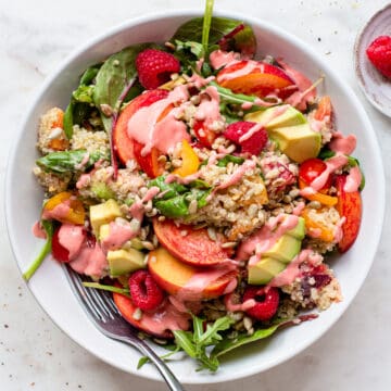 Quinoa salad with avocado, peaches, tomatoes and raspberries in a white shallow plate.