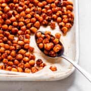 Spoon with roasted chickpeas on a white baking tray.
