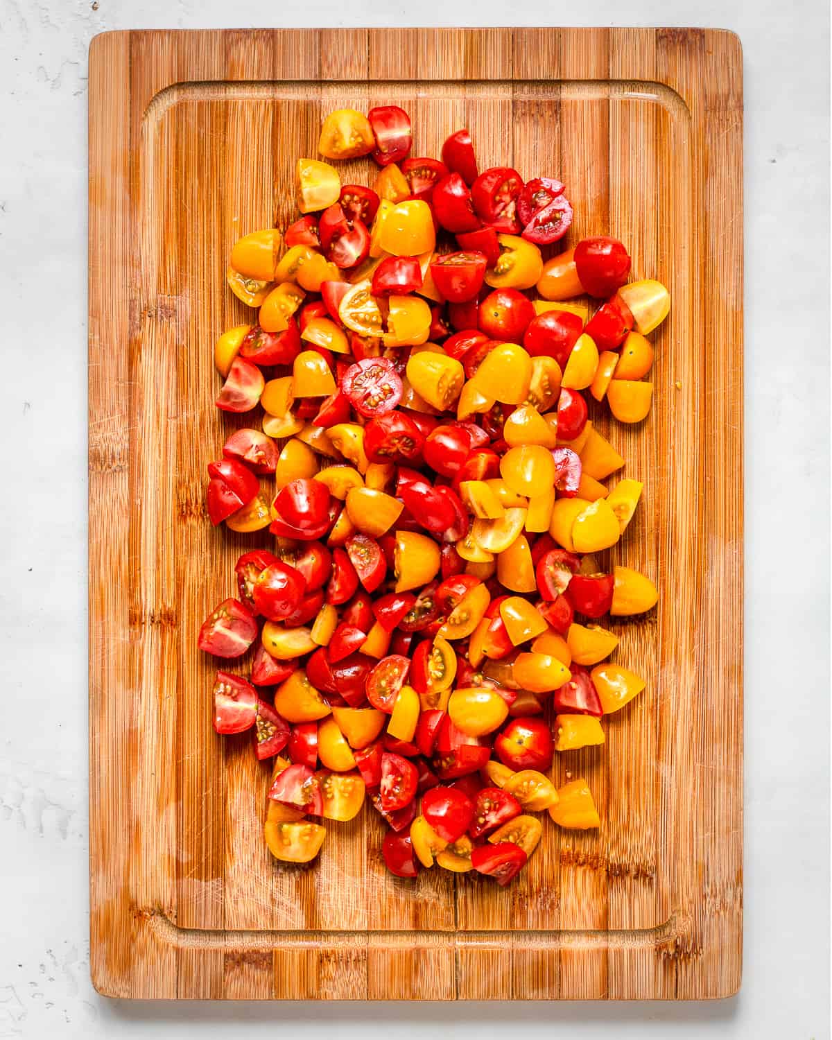 Chopped red and yellow cherry tomatoes on a wooden cutting board.