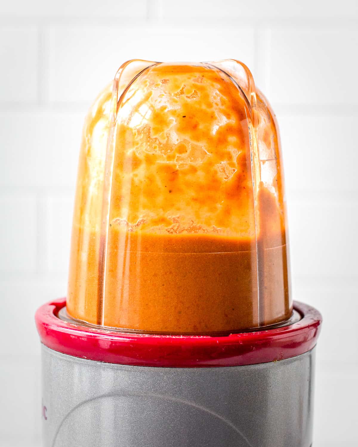 Orange dressing made from sun-dried tomatoes and capers in a blender jar.