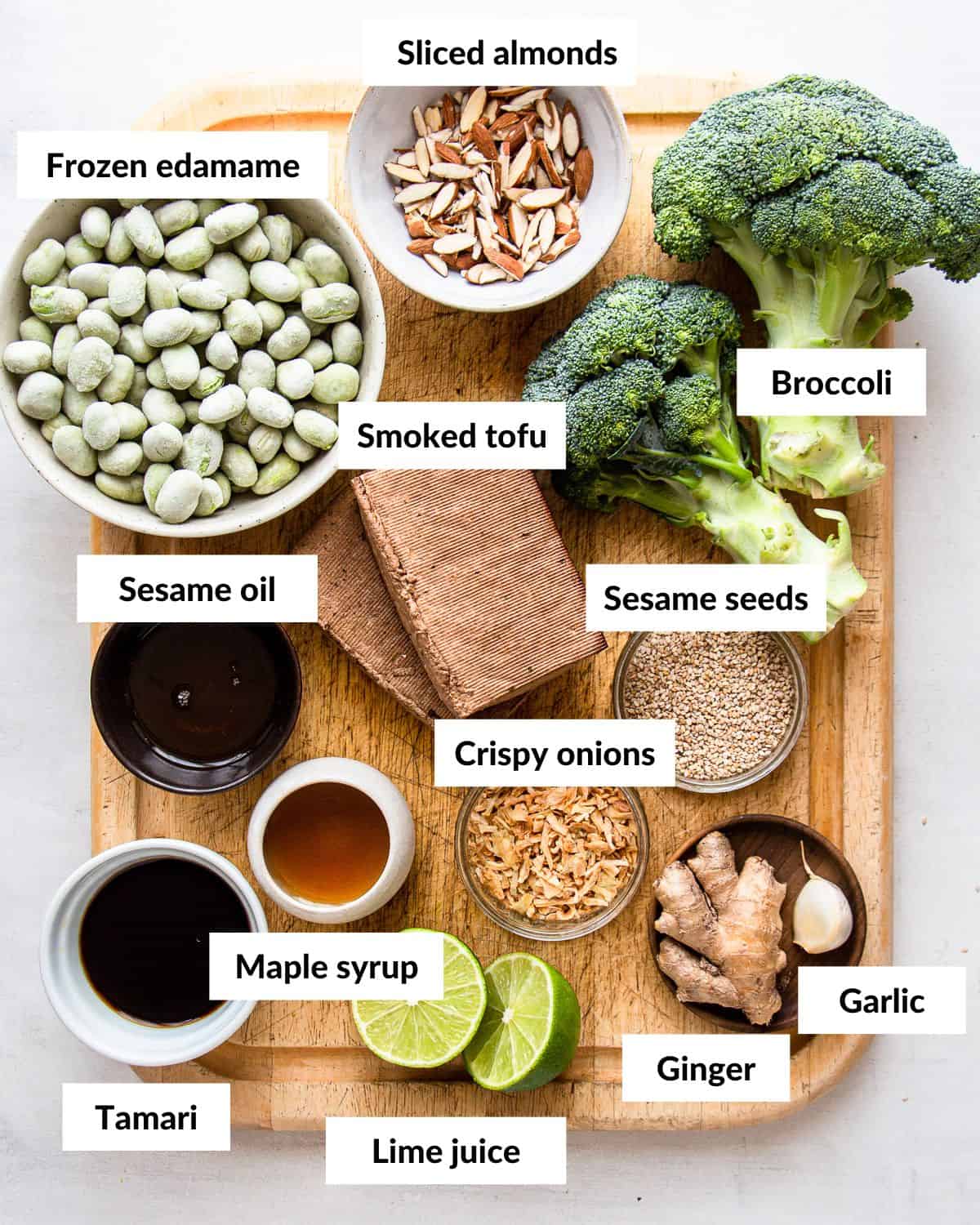 Ingredients for a raw broccoli salad on a wooden cutting board with descriptive labels.
