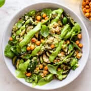 Roasted zucchini salad with quinoa, chickpeas and a green dressing in a white shallow plate.