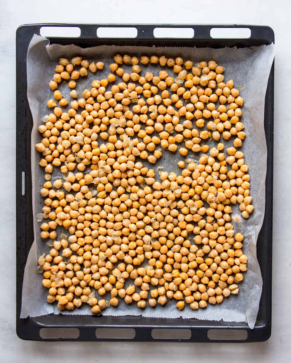 Seasoned chickpeas on a parchment linked baking tray.