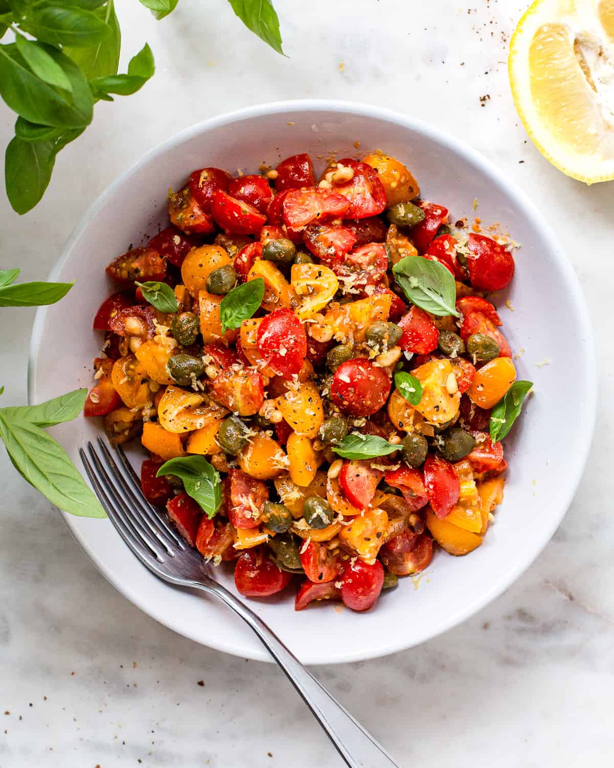 Tomato and caper salad with basil and lemon zest in a white bowl.