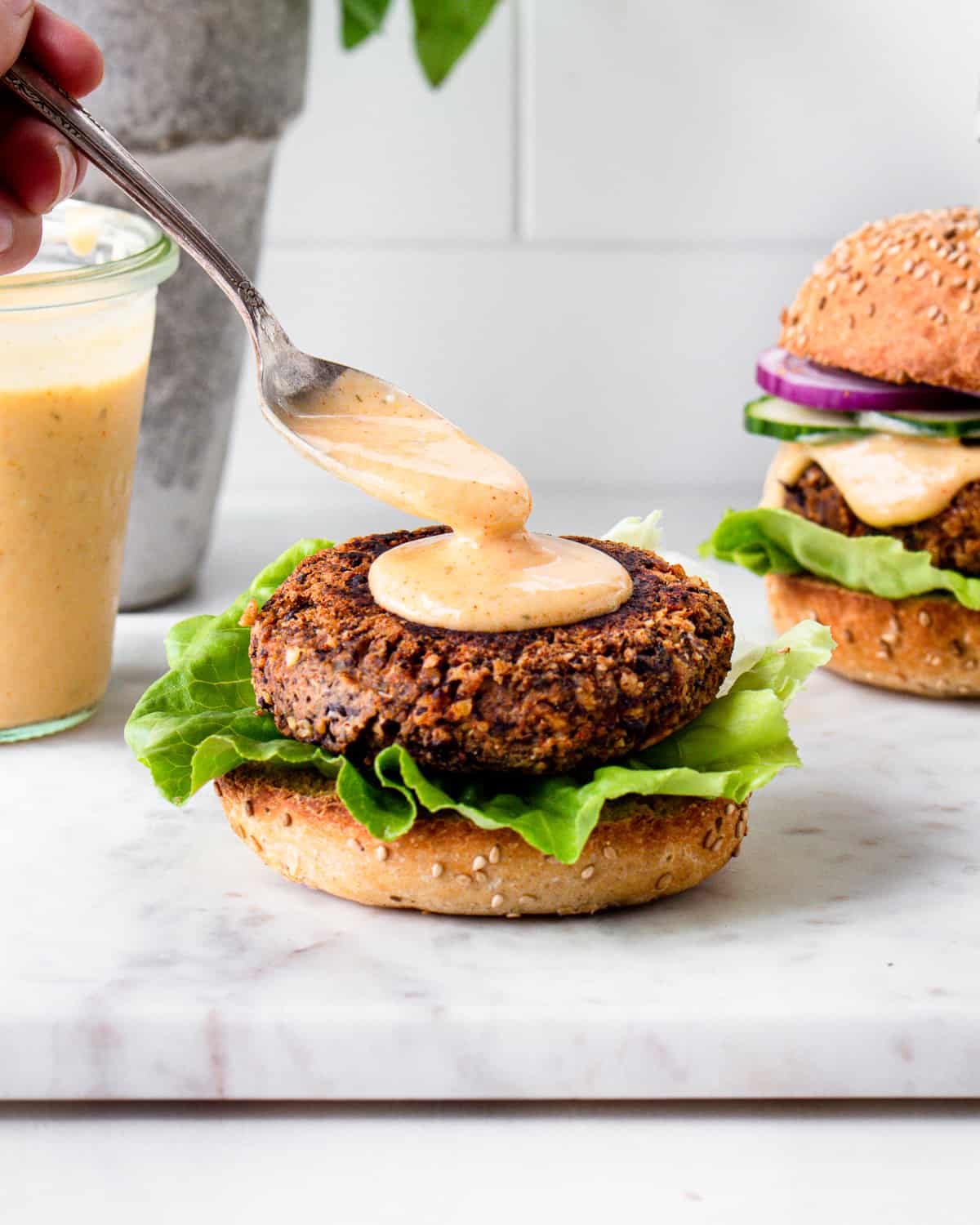 Hand spooning some burger sauce on a veggie burger patty.