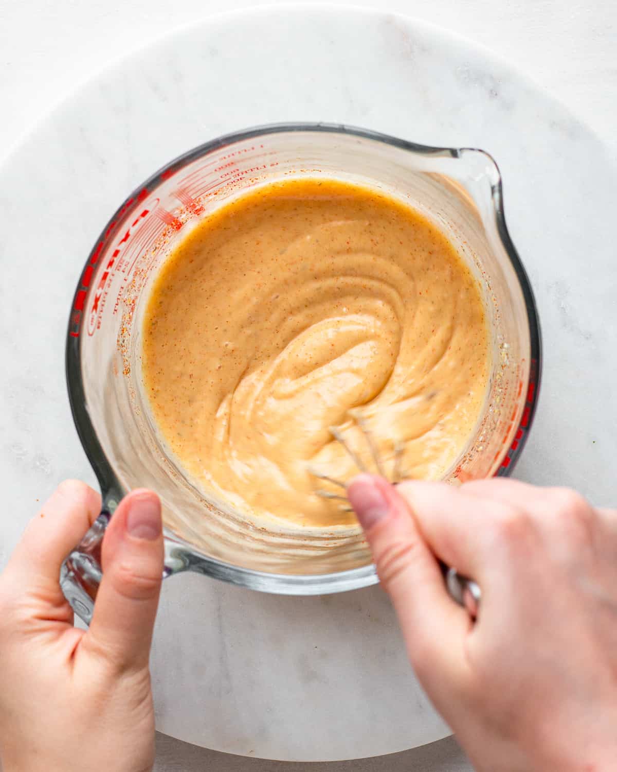 Hand whisking an orange burger sauce in a glass bowl.