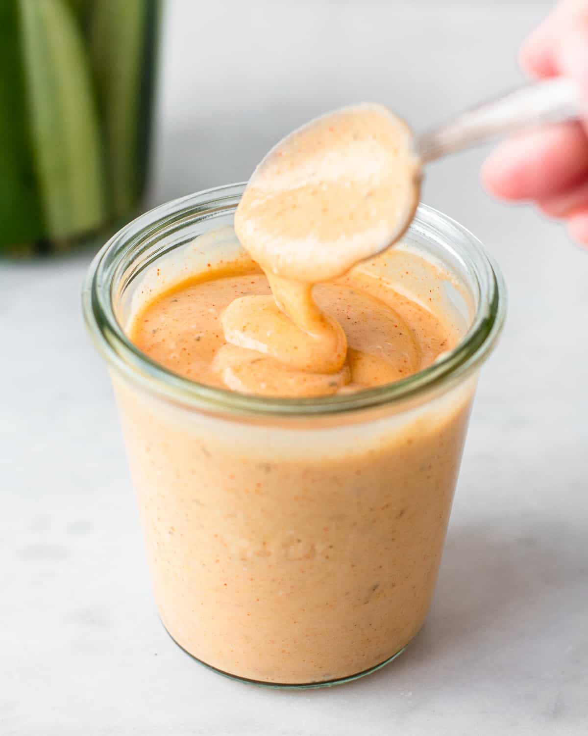 Hand spoon an orange veggie burger sauce in a glass jar.